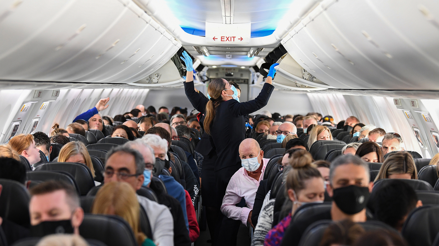 Flight attendants close overhead bins in a plane cabin.